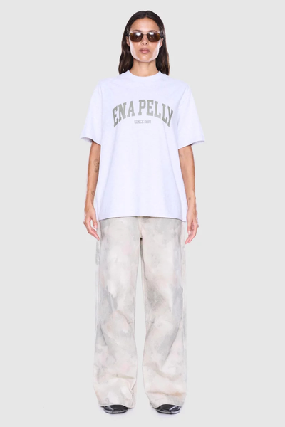Full-length studio front shot of a model wearing tinted sunglasses, a white marle graphic t-shirt, and relaxed patterned wide-leg pants.