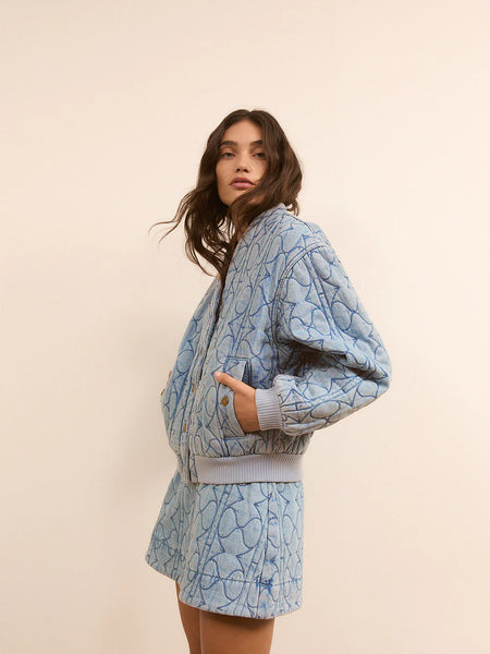 A front lifestyle studio image of the heavy-weight quilted jacket styled open over a white tank top, emphasizing its relaxed, off-duty drape against the body.