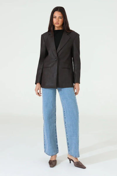 A full-length front studio shot of the model standing forward with one hand resting in her jean pocket, showcasing the open styling potential of the fully lined chocolate brown oversized blazer.