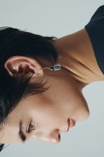Side profile shot of a model wearing the Temple of the Sun Aqua Earring in 18k Gold Vermeil, highlighting the slender hook drop and blue topaz stones.