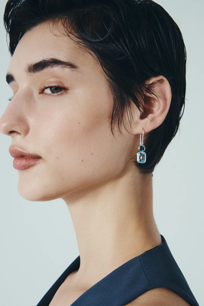 Profile side shot of a model wearing a Temple of the Sun Aqua Earring in Sterling Silver showing the drop fit and blue topaz gemstones.