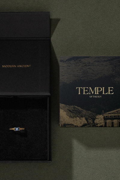Flat-lay shot of the Temple of the Sun jewelry box packaging and printed card on a dark green surface.