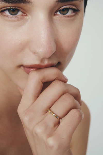 Close-up shot of a model holding her hand near her face, wearing the Temple of the Sun 18k Gold Vermeil Aqua Ring with five teal topaz stones.