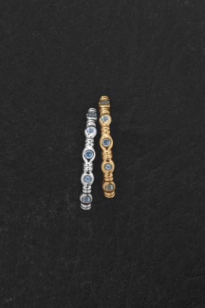 Overhead view of the Temple of the Sun Aqua Ring shown in both 18k Gold Vermeil and Sterling Silver variations side-by-side on a dark textured surface.