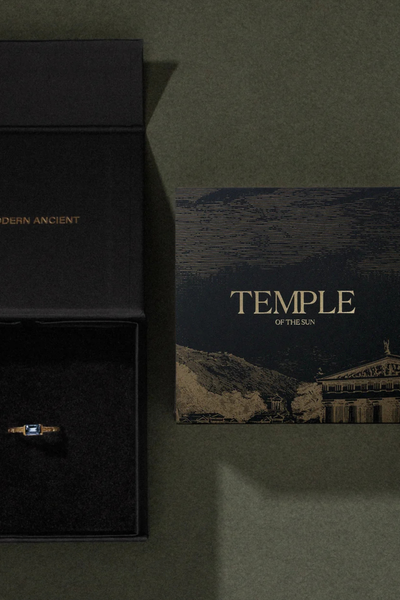 Overhead shot of a dark green Temple of the Sun branded jewelry box and artwork card displaying a ring inside.