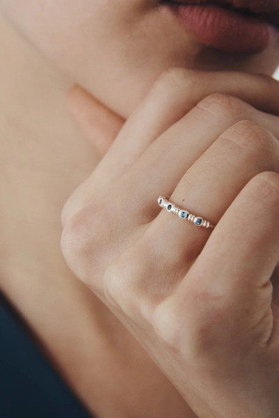 Close-up of a model holding her hand near her face, wearing the Temple of the Sun Sterling Silver Aqua Ring with five teal topaz gemstones on her finger.