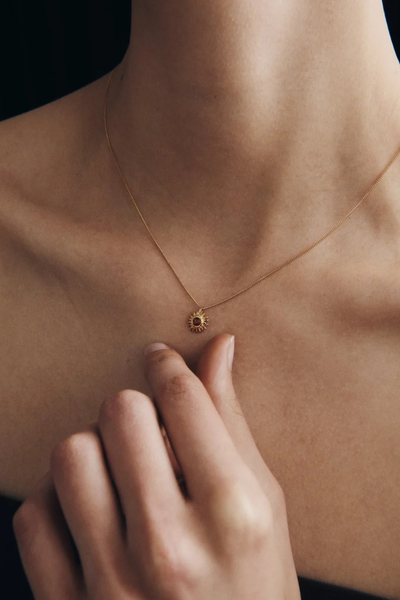 Close-up shot of a model wearing the Temple of the Sun Aten Necklace in 18k Gold Vermeil, displaying the orange garnet pendant resting against the collarbone.