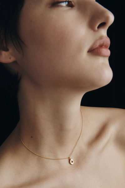 Profile view of a model wearing the Temple of the Sun Blaze Coin Necklace in 18k Gold Vermeil resting gently on the collarbone.