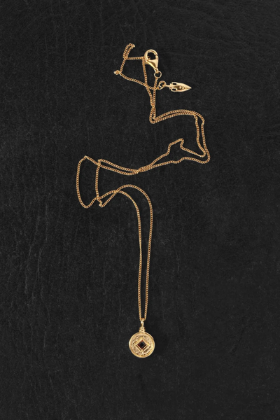 Flat-lay view of the Temple of the Sun Blaze Coin Necklace in 18k Gold Vermeil laid out on a dark textured surface, showing the chain, clasp, and coin pendant.