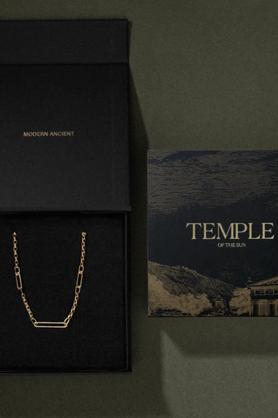 Top-down packaging view of an open black Temple of the Sun branded gift box and art card on a green surface.