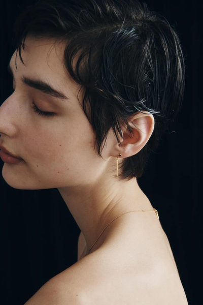 Side profile shot of a model wearing a Temple of the Sun Cinder Earring in 18k Gold Vermeil against a dark backdrop.