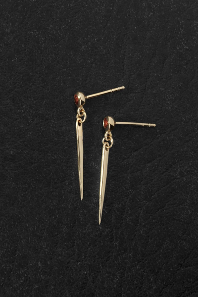 Flat-lay view of the Temple of the Sun Cinder Earrings in 18k Gold Vermeil laid out on a dark textured surface, showing the stud posts and spike drops.