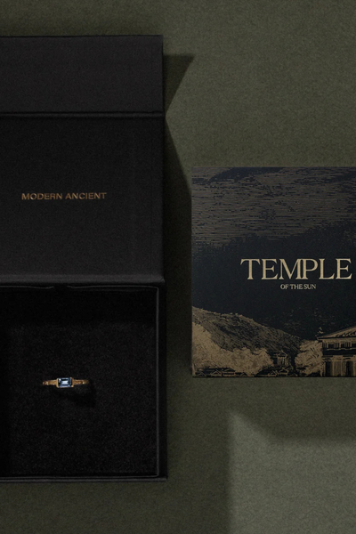 Overhead view of an open black Temple of the Sun branded gift box and illustrated art card on a dark green surface.