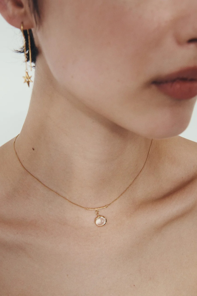 Lifestyle shot of a model wearing the Temple of the Sun Electra Star Threader Earrings paired with a gold pendant necklace.