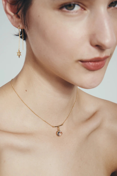Close-up profile of a model wearing the Temple of the Sun Electra Star Threader Earring alongside a delicate gold charm necklace.