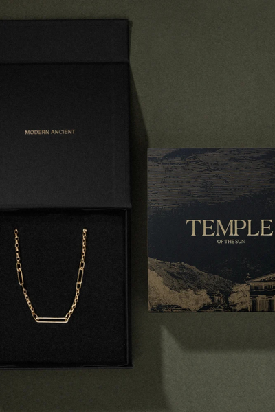 Top-down packaging view of an open black Temple of the Sun jewelry box and printed artwork card on a textured green surface.
