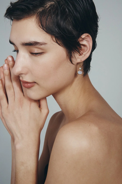 Profile view of a model with hands folded, wearing the Temple of the Sun Ether Earring in 18k Gold Vermeil.