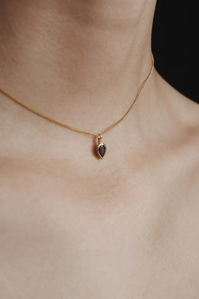 Extreme close-up view of the pear-cut garnet pendant and gold bezel setting of the Temple of the Sun Ignis Necklace worn by a model.