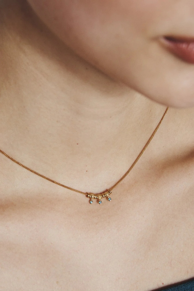 Close-up lifestyle photo of a model wearing the delicate Temple of the Sun Isla Necklace with London Blue Topaz drops.