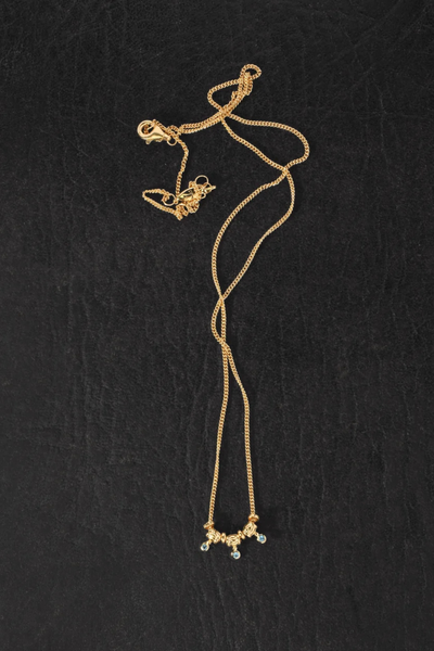Overhead product photo of the Temple of the Sun Isla Necklace in 18k Gold Vermeil laid out on a dark textured surface showing the clasp and extension chain.