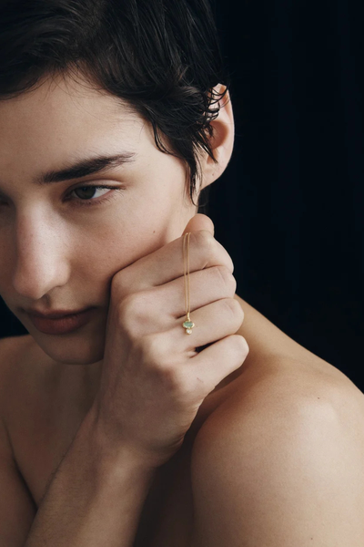 Profile photo of a model holding the Temple of the Sun Ma Necklace in 18k Gold Vermeil near her cheek.