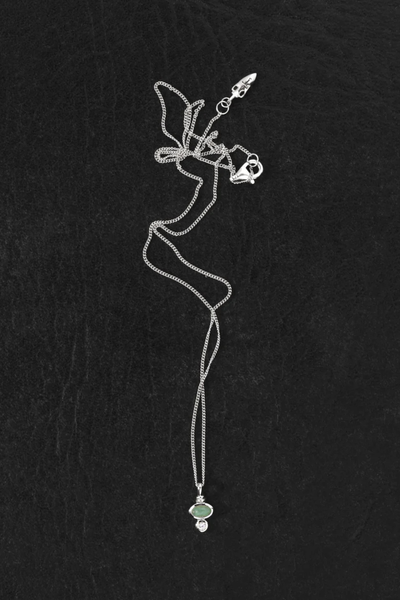 Flat-lay view of the delicate Temple of the Sun Ma Sterling Silver chain and pendant on a dark background.