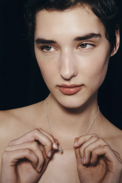 Close-up side profile of a model displaying the small silver Ma pendant on the collarbone.