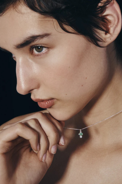 Close-up side profile of a model displaying the small silver Ma pendant on the collarbone.