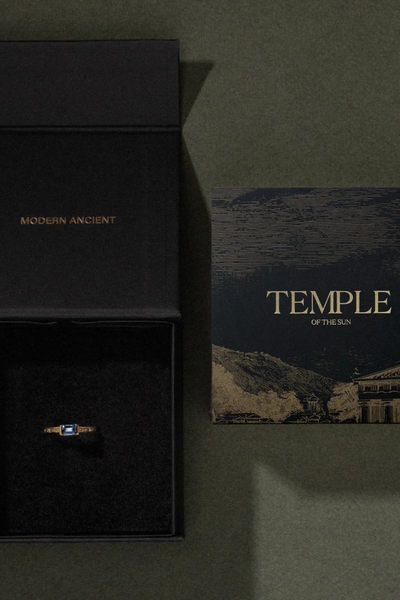 Top view of an open black Temple of the Sun branded gift box beside an artwork card on a dark green surface.