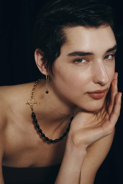 Close-up lifestyle photo of a model resting her face against her hand, wearing the Temple of the Sun Sela Earring in 18k Gold Vermeil.