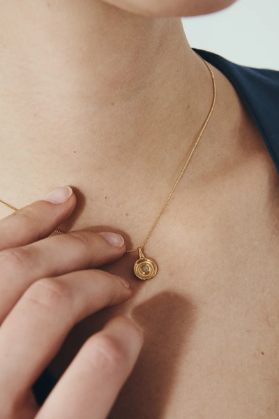 Close-up photo of a model holding the Temple of the Sun Soma Coin pendant against her chest.