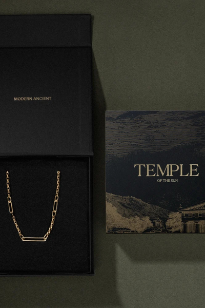 Top-down view of an open black Temple of the Sun branded gift box displaying a chain beside an artwork card on a dark background.