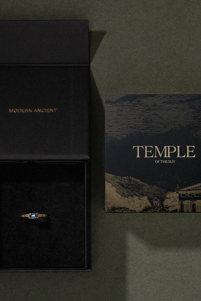 Top-down view of an open black Temple of the Sun branded gift box beside an artwork card on a dark green surface.