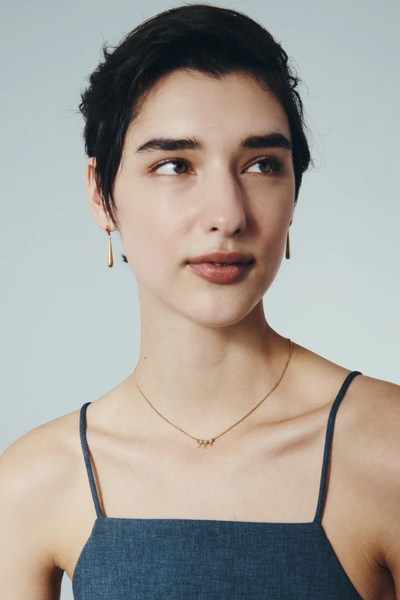 Three-quarter portrait shot of a model displaying the gold Stilla drop earrings against a light background.