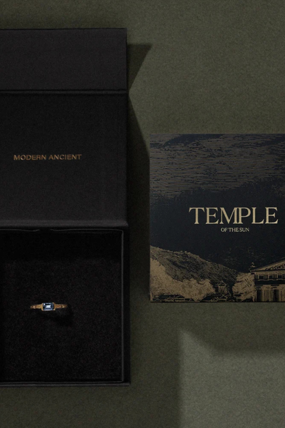 Top view of an open black Temple of the Sun branded gift box beside an artwork card on a dark surface.