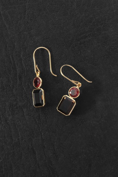 Top-down product photo of the Temple of the Sun Umber Earrings in 18k Gold Vermeil resting on a dark textured surface.