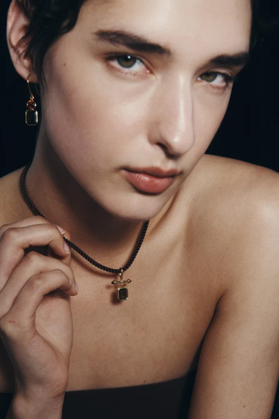 Direct shot of a model touching her corded necklace while wearing the Temple of the Sun Umber Earrings in 18k Gold Vermeil.