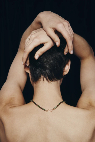 Back view shot of a model showing the gold S-hook clasp of the Temple of the Sun Vana Beaded Necklace resting on the nape of the neck.