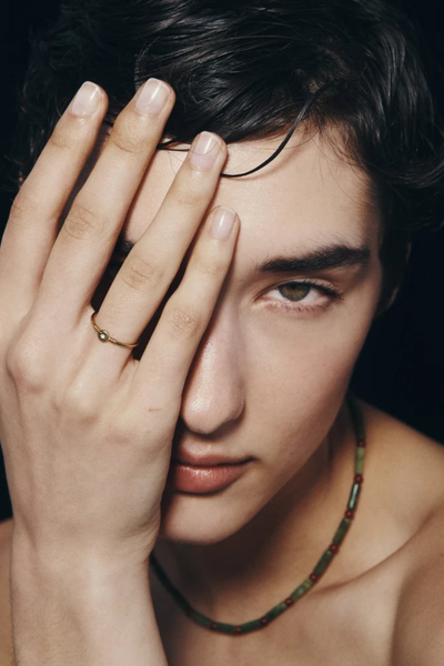 Close-up portrait of a model wearing the Vana Beaded Necklace while resting her hand across her face displaying a gold ring.