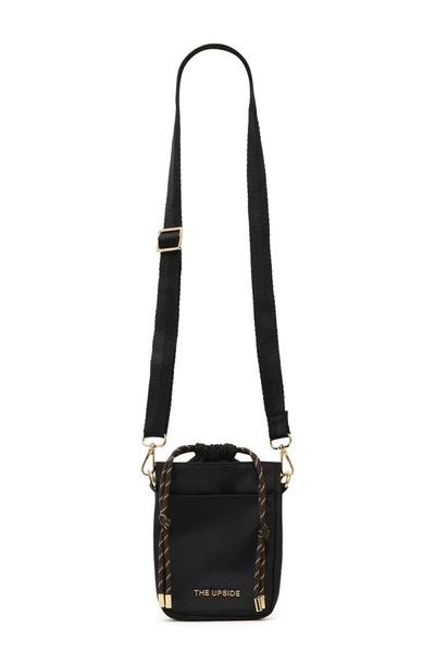 Studio front view of a small black recycled polyester crossbody bag featuring a front slip pocket, internal drawstring opening with patterned paracord, gold "THE UPSIDE" metallic logo, gold hardware, and an adjustable, removable black webbed shoulder strap.