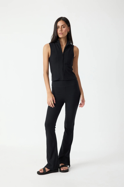 Full-length studio front view of a model wearing the black flare pants and matching black sleeveless zip-up top, paired with sandals.