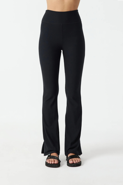 Studio front view of a model wearing the black Divina Florence flare pants with hem splits and sandals.
