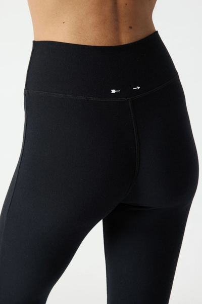 Close-up rear view of the waistband on the black flare pants, showing the small printed cream arrow logos at the back.