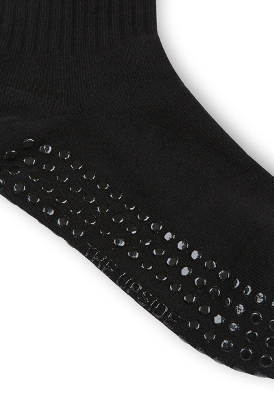 Close-up studio shot of the black anti-slip grip sock, highlighting the textured rubber grips on the sole and the debossed "The Upside" logo along the bottom.