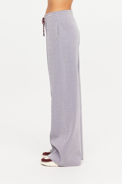 Side profile studio shot of a model wearing the Galaxia Marnie Wide Leg Pants in Starry. This angle highlights the clean side seam lines, functional pockets, and the effortless, straight-leg pooling over deep maroon and cream athletic sneakers.