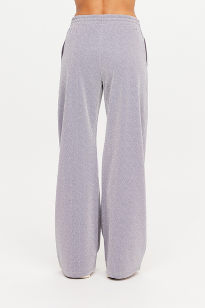 Rear studio view of a model wearing the high-rise Galaxia Marnie Wide Leg Pants. The shot emphasizes the comfortable elasticated waistband and the subtle, shimmering texture of the grey Lurex and polyester blend fabric.