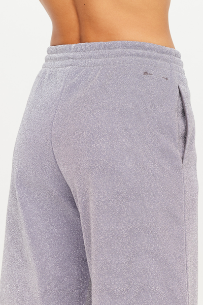 Close-up rear shot of the Galaxia Marnie Wide Leg Pants in Starry. The image highlights the fine, glittering knit texture of the Lurex fabric, a side pocket slit, and the brand's signature arrow logo embroidered in tonal grey thread below the elastic waistband.