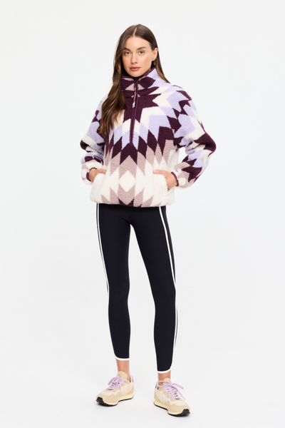 Full-length front view of model Eden wearing the relaxed geometric star print Harlow Fleece Pullover in Maple Chaud by The Upside, paired with black side-stripe leggings and sneakers.