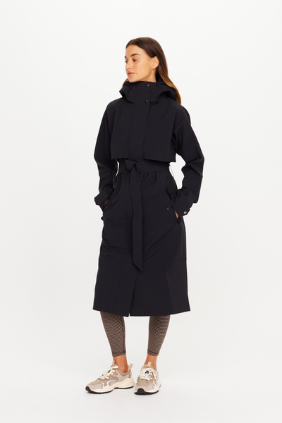 Three-quarter front studio view of the model wearing the black sand James Hooded Trench Coat fully closed. The image highlights the adjustable waist belt tied securely, the clean storm flap overlay, and the high-neck stand collar with a built-in hood for ultimate weather protection.