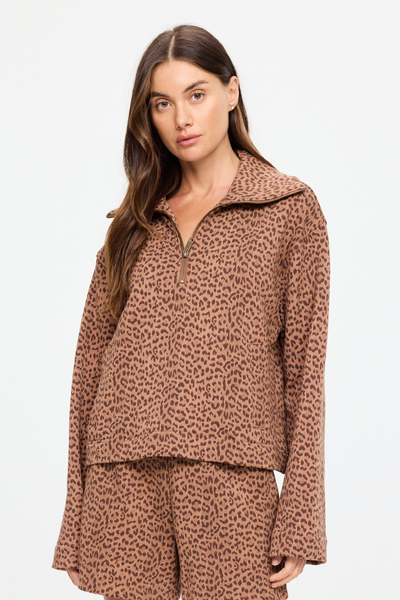 Half-length studio shot of a model wearing the Javan Jones Quarter Zip Sweat in a warm brown leopard print. The image highlights the relaxed fit, dropped shoulders, and the open collar styled with the zipper halfway down.